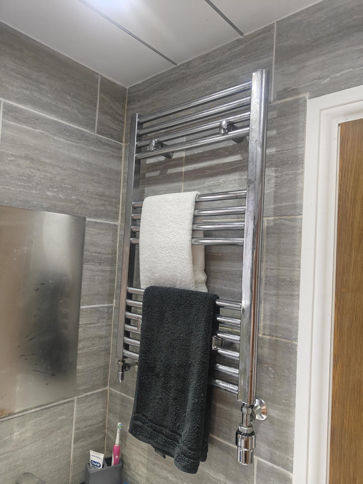 Chrome ladder towel radiator against grey bathroom tiles